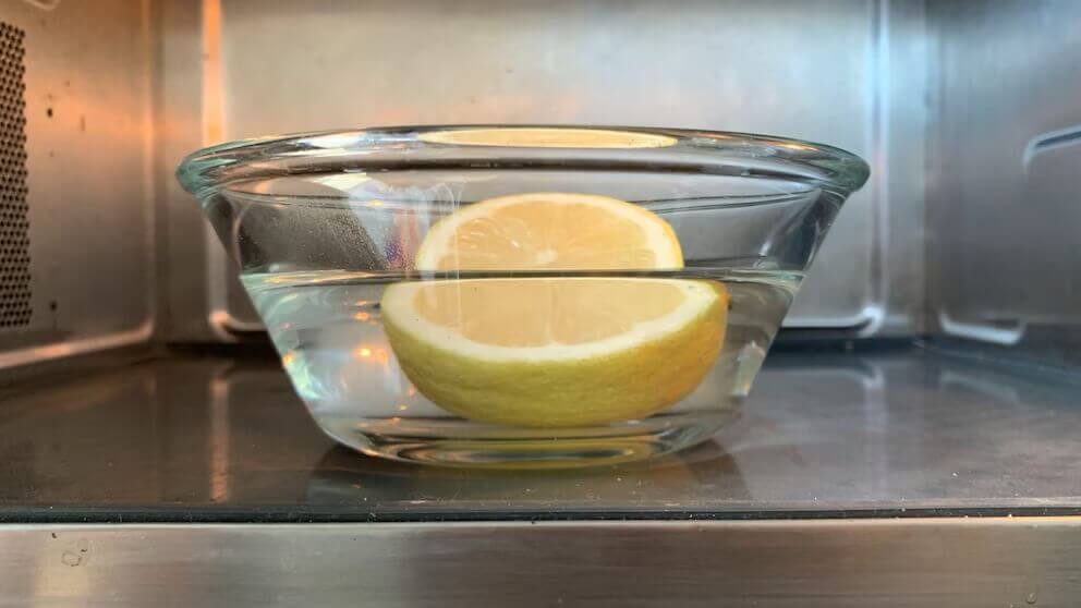 Glass bowl with water and a halved lemon inside a microwave