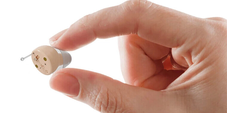 Close-up of a person's hand holding a small, flesh-colored hearing aid device