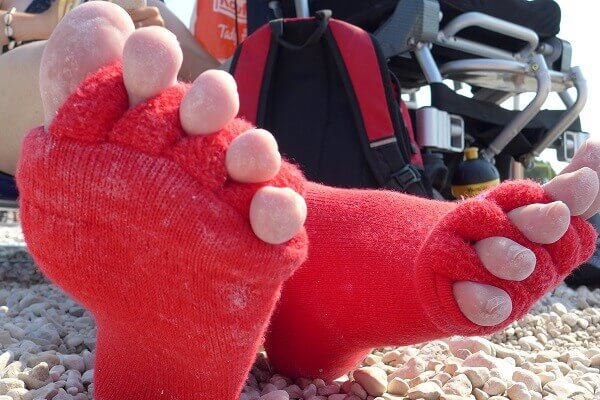 Feet wearing bright red toe-separating socks on a pebble surface