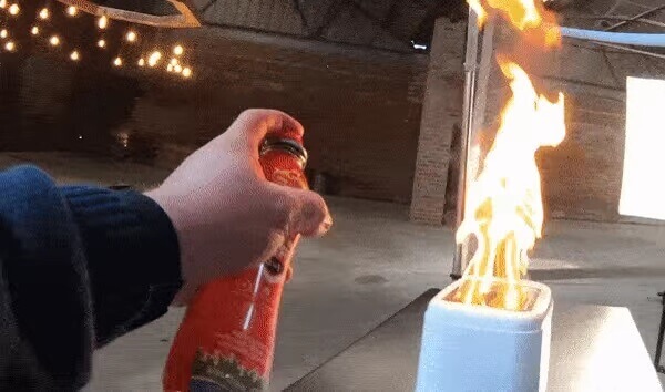 Person using a small fire extinguisher to put out a fire in a white container