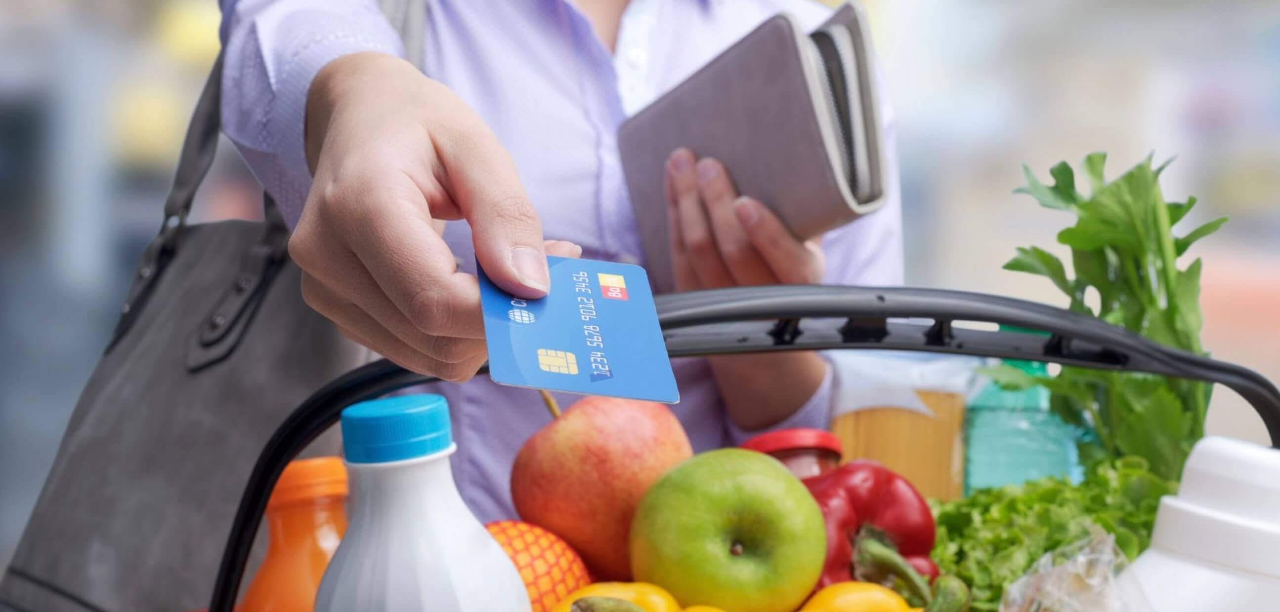 Person holding a credit card over a basket of groceries