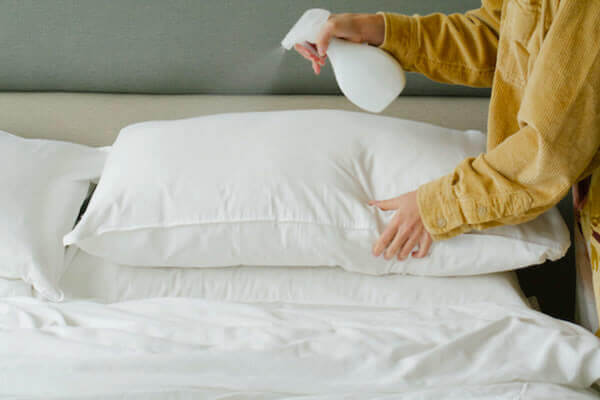 Person spraying a white pillow on a bed with a spray bottle